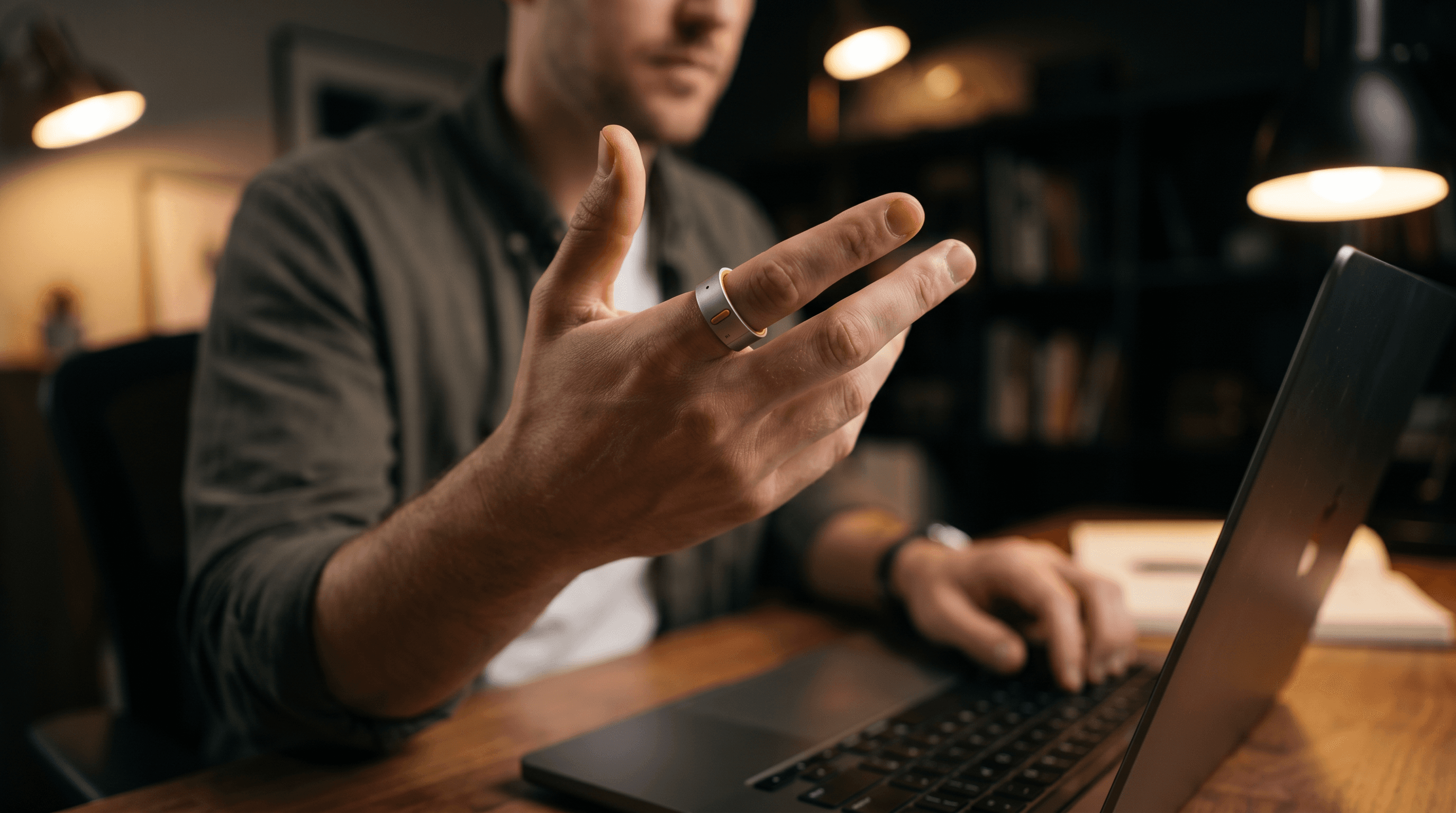 A person at a desk wearing the Rhyme Devices R1 ring on their index finger, mid-gesture beside an open laptop