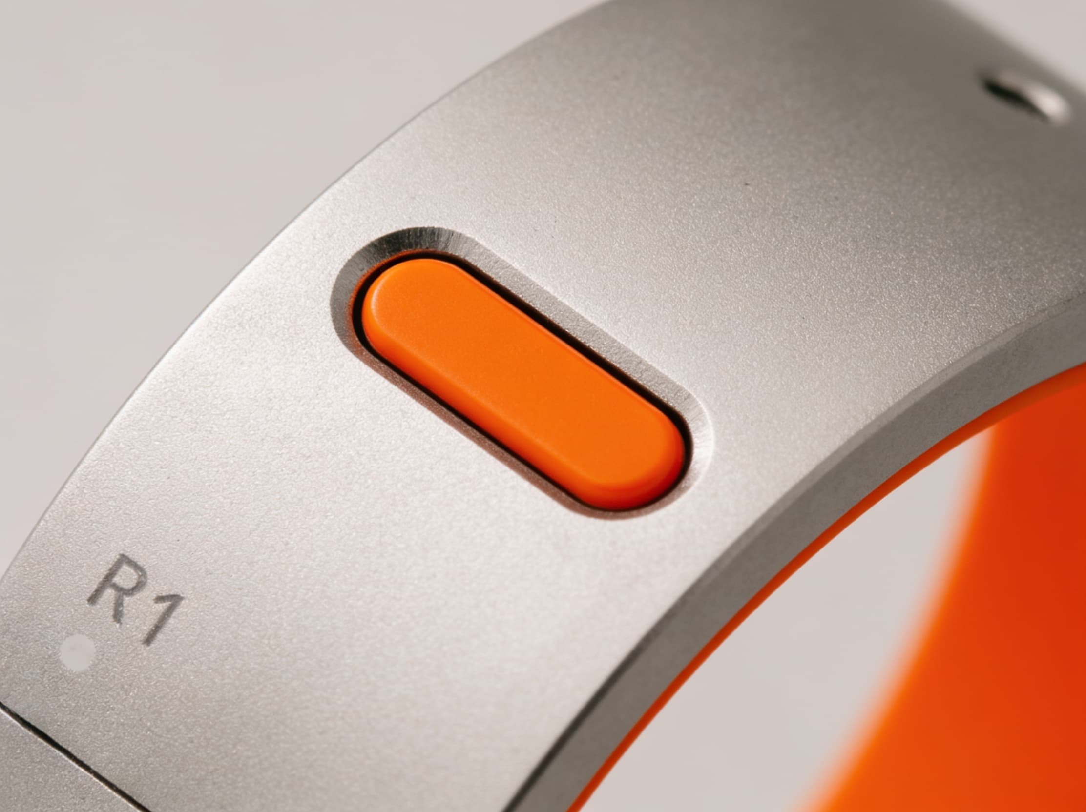 Macro close-up of the Rhyme Devices R1’s recessed oval button and microphone mesh on the brushed silver band
